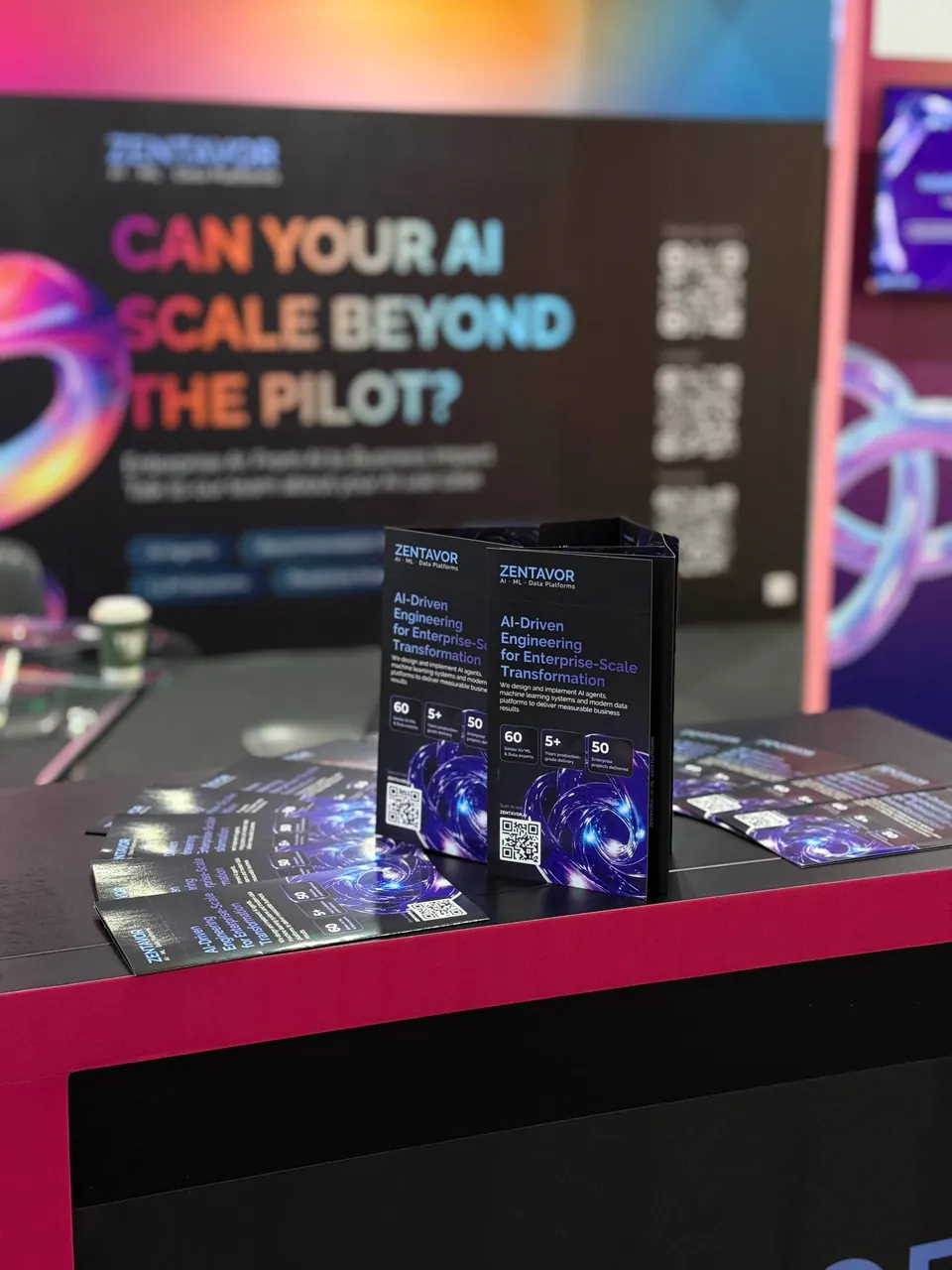Zentavor brochures on the stand counter, the banner “Can your AI scale beyond the pilot?” behind them