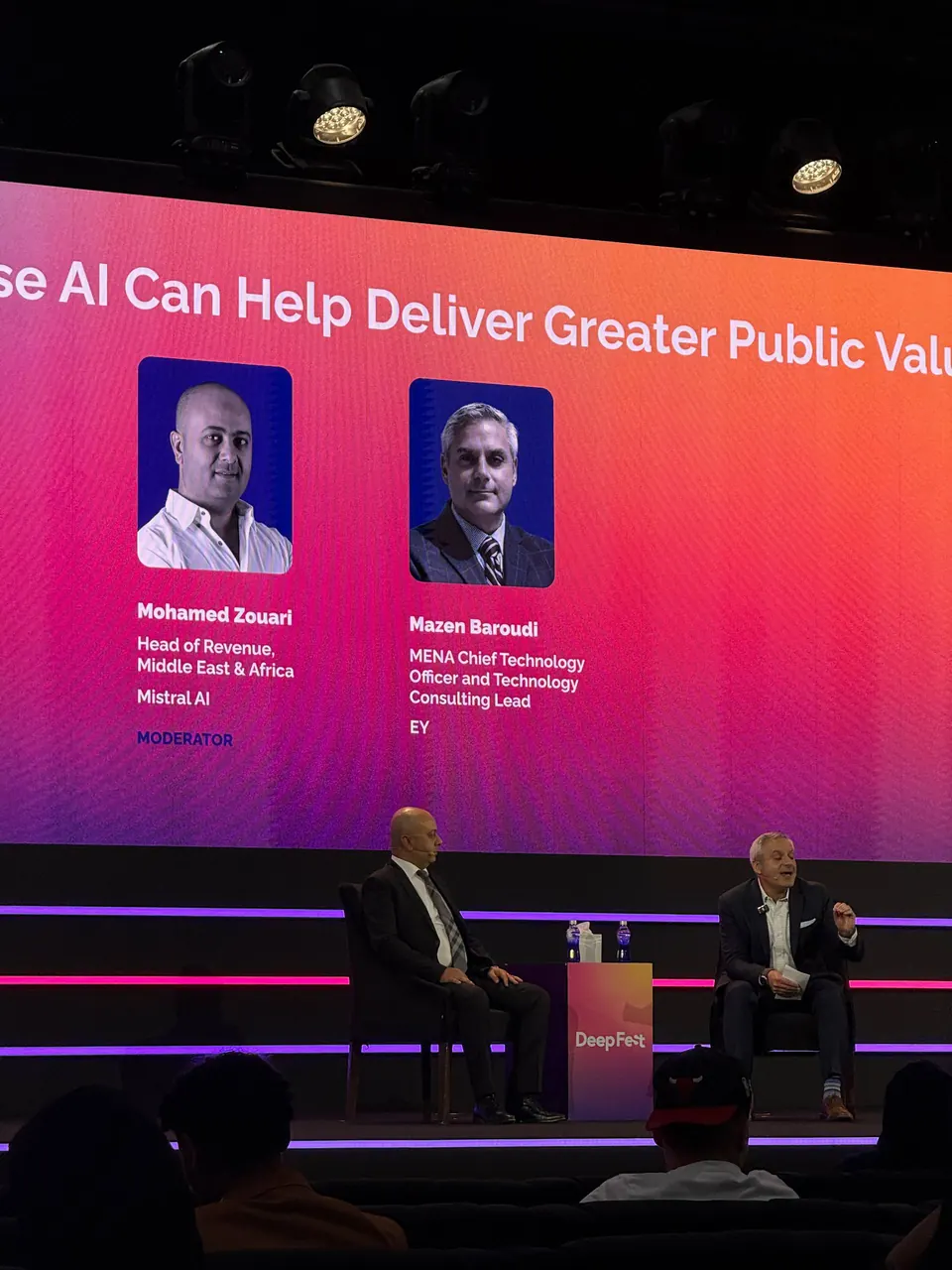 Two panelists on a DeepFest stage in front of a large screen with the session title